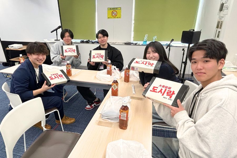 ナゴグルさんお勧めの「大衆韓国」のお弁当を持つ参加者たち